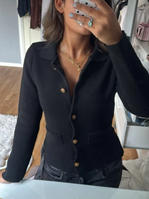 Svart figursydd kofta med guldknappar - Stilren svart kofta med figurnära passform och snygga guldknappar framtill från zara. Koftan har krage och två dekorativa fickor. Perfekt för en trendig och elegant look. I nyskick