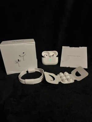 Apple AirPods Pro 2 trådlösa hörlurar - Säljer ett par vita Apple AirPods Pro2 med laddningsetui, extra silikonpluggar och laddningskabel. Hörlurarna har en stilren och kompakt design i plast och levereras i originalförpackning. Perfekta för musik, samtal och träning.
