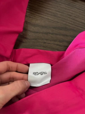 Helt ny rosa shoppingväska från HEDABAG - Snygg och rymlig shoppingväska i starkt rosa tyg från Hedabag. Väskan har bred axelrem och kommer med en matchande liten påse. Perfekt för att bära med sig allt man behöver. Materialet känns slitstarkt och väskan har en enkel, modern design.