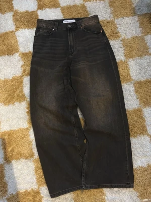 Bershka baggy jeans  - Säljer ett par bruna jeans med loose fit och hög midja. Jeansen har raka ben, klassiska fem fickor och knappgylf. Materialet är denim i bomull och färgen har en lätt tvättad look för en cool vintagekänsla.