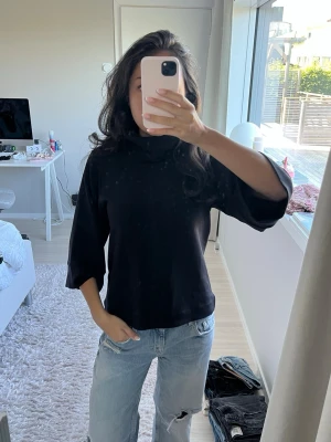 Svart polotopp med trekvartsärm - Snygg svart polotopp med lös passform och trekvartsärmar från InWear!! Toppen har en hög krage och är tillverkad i ett mjukt material som känns bekvämt mot huden. Perfekt att styla med jeans eller kjol för en clean look.