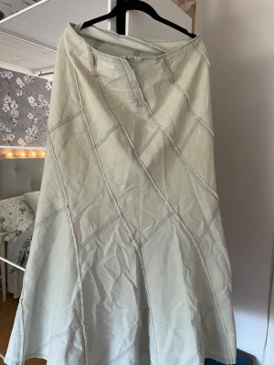 Ljusbeige långkjol med patchwork - Säljer en ljusbeige långkjol med patchwork-design och synliga sömmar i ett rutmönster. Kjolen har en lätt utsvängd form och stängs med dragkedja fram. Perfekt för dig som gillar en unik och avslappnad stil. Denna är också vintage