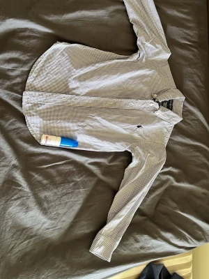Rutig skjorta från Ralph Lauren - För barn. Klassisk rutig skjorta från Ralph Lauren i vitt och mörkblått. Skjortan har lång ärm, knappar framtill och den ikoniska loggan broderad på bröstet. Tillverkad i mjuk bomull som känns skön mot huden. Perfekt för en stilren och avslappnad look.