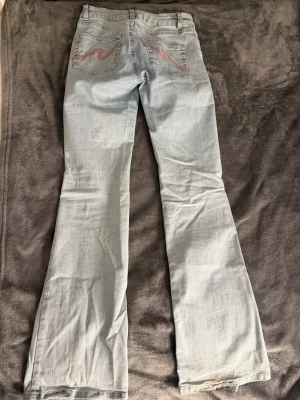 Ljusblå bootcut jeans med slitningar - Säljer ett par ljusblå bootcut jeans med slitna knän och broderade detaljer på bakfickorna. Köptes för 700kr och är använda 2 gånger. Storlek 38 men passar även 36. Jeansen har klassisk femficksmodell och är tillverkade i denim med lätt stretch. Perfekta för en avslappnad och trendig look.