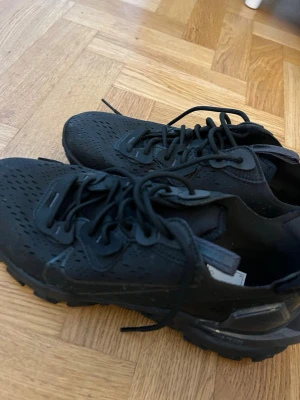 Svarta Nike React sneakers med grov sula - Säljer ett par helsvarta Nike sneakers med perforerat material och robust, mönstrad yttersula. Skorna har lågt skaft, klassisk snörning och diskret Nike-logga på sidan. Perfekta för dig som gillar sportig och stilren look. Använda 1 gång. 