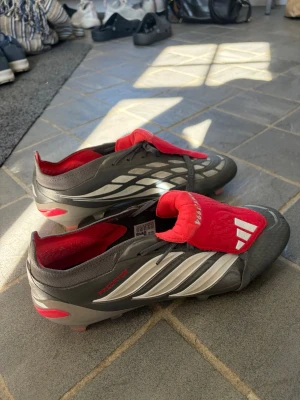Adidas Predator fotbollsskor silver/röd - Säljer ett par Adidas Predator Elite Fold-Over FG i färgen Finishers Steel (grå/röd).  Skorna är i storlek 45⅓ och har endast använts 2-3 gånger pga att det va för små för mig. De är i mycket fint skick. Inga större skador eller fel. Nypris: ca 3 200 kr.  Mitt pris: 1799✅