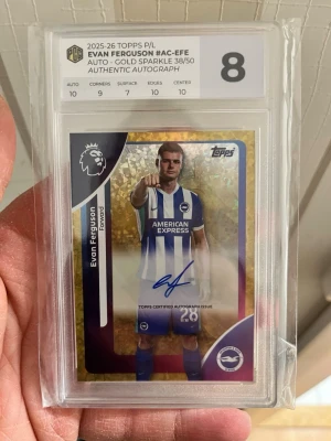 Topps autografkort Evan Ferguson 38/50 - Säljer ett exklusivt Topps autografkort av Evan Ferguson från Brighton & Hove Albion, Premier League 2025/26. Kortet är Gold Sparkle-variant, numrerat 38/50 och graderat 8 av PCG. Kortet har en autentisk autograf och levereras i skyddande plastfodral.