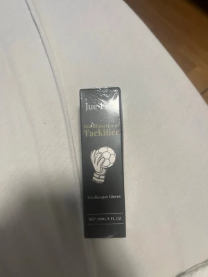 Jue-Fu klister för målvaktshandskar - Multifunktionellt klister från Jue-Fu för målvaktshandskar. Förpackningen är svart med vit text och illustration av en handske som håller en boll. Innehåller 30 ml och används för bättre grepp vid spel.