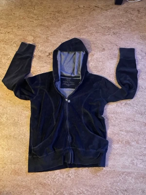Grå/svart Y2K tröja - Snygg grå/svart tröja i mjuk velour. Tröjan har dragkedja framtill, två fickor och en fodrad huva med grå insida. Perfekt för en chill och avslappnad stil. Passar till både jeans och mjukisbyxor. Snören finns ej.