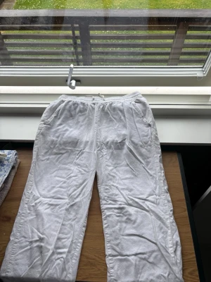 Vita linnebyxor med resårmidja - Säljer ett par vita linnebyxor med avslappnad passform och resår i midjan. Byxorna har två sidofickor fram och en bakficka. Perfekta för en chill och luftig stil under varma dagar.