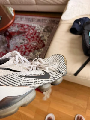 Vita och svarta sneakers med mönster - Snygga sneakers i vitt med svarta ränder och detaljer. Skorna har en stickad ovandel och genomskinlig sula med synliga luftbubblor. De har snörning och en sportig look som passar till streetwear. Perfekta för dig som gillar modern och bekväm stil. Dom är lite paffa där back 