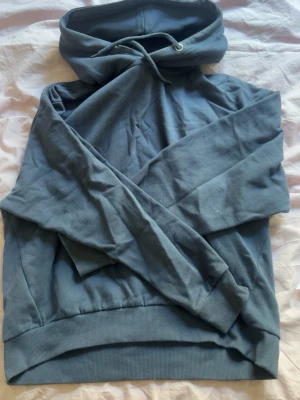 Blå hoodie med huva och dragsko - Mysig blå hoodie med huva och dragsko. Tillverkad i mjukt bomullsliknande material och har ribbade muddar vid ärmslut och nederkant. Perfekt för en avslappnad och chill stil.