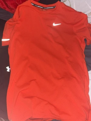 Röd tränings-tshirt från Nike - Snygg röd tränings-tshirt från Nike med klassisk vit logga på bröstet. Tillverkad i ett lätt och ventilerande funktionsmaterial som passar perfekt till träning. T-shirten har rund halsringning och korta ärmar.