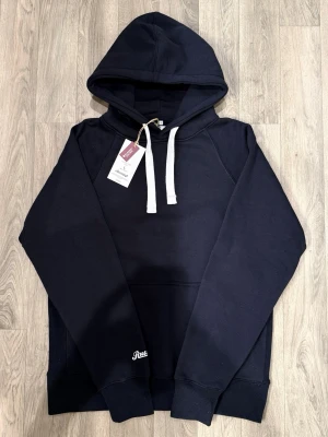 Russemerch Hoodie Navy Strl L - Ny med prislapp - Russemerch navy hoodie med klassisk passform, ny med prislapp, storlek L, bröstvidd 55 cm, armlängd 79,5 cm, midja 50 cm, längd 70 cm, i nyskick.