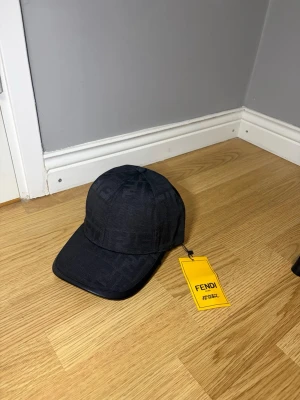 Svart keps från Fendi med logomönster - Snygg svart keps från Fendi med diskret ton-i-ton logomönster över hela kepsen. Klassisk böjd skärm och justerbar baksida. Tillverkad i ett slitstarkt tygmaterial som ger en exklusiv känsla. Perfekt accessoar för att lyfta din outfit.