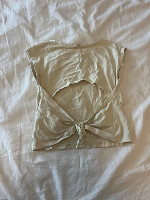 Beige topp med öppen rygg och knyt - Trendig beige topp i bomull med öppen rygg och knyt i midjan. Använd fåtal gånger.
