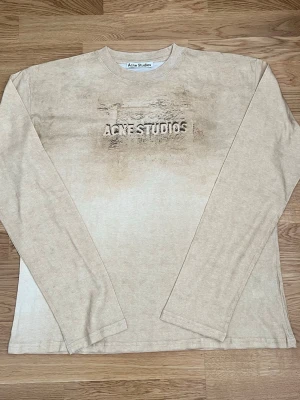 Beige långärmad tröja Acne Studios - Snygg beige långärmad tröja från Acne Studios med unikt texturtryck och logga framtill. Tröjan har rund halsringning och är gjord i mjukt material, perfekt för en avslappnad och trendig stil.