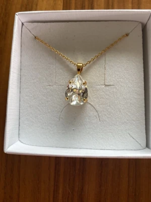 Guldhalsband med droppformad kristall diamantslipad! - Snyggt halsband från Caroline Svedbom med en tunn guldfärgad kedja och en stor, droppformad klar kristall som hänge. Perfekt för dig som gillar stilrena och eleganta smycken med lite extra bling.