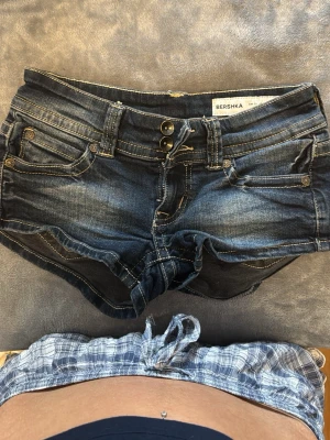 Mörkblå jeansshorts från Bershka - Snygga mörkblå jeansshorts från Bershka med dubbla knappar och klassiska fickor. Shortsen har låg midja och slitna detaljer för en cool look. Pris kan diskuteras 