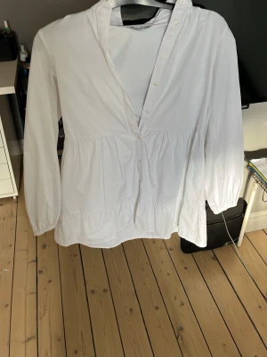 Vit volangklänning med knappar - Säljer en vit klänning i bomull med lång ärm och knappar framtill. Klänningen har volangdetaljer och en loose passform som ger en avslappnad och trendig vibe. Perfekt för dig som gillar stilrena och enkla plagg.