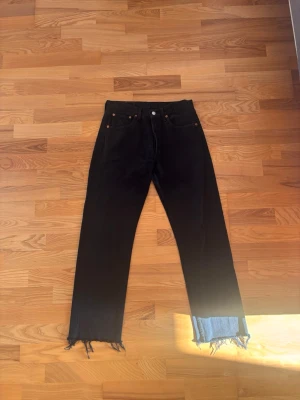 Levi’s 501 Vintage 90s – Black – W31 L32 – Europe Made (252) - Snygga Levi’s 501 i svart denim, klassisk passform och äkta “distressed” look. Storlek W31 L32. Jeansen har fransade benslut, lätt slitage i grenen och en mindre lagning, men allt är stabilt och ger ett råare vintage-inspirerat uttryck.  Perfekta för dig som gillar en mer worn-in stil och äkta karaktär i denim. 