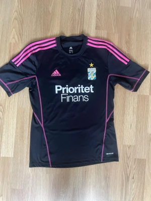 Retro IFK Göteborg matchtröja Adidas - Säljer en svart IFK Göteborg matchtröja från Adidas med rosa detaljer och klubbmärke på bröstet. Tröjan har korta ärmar, rosa ränder på axlarna och tryck med sponsor på framsidan. På ryggen står det 'valgardsson' och nummer 3. Material: polyester.