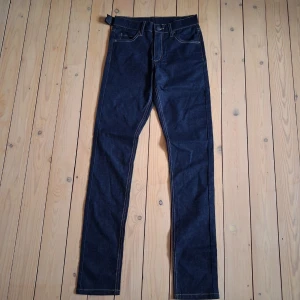 Mörkblå raka jeans med kontrastsömmar - Snygga mörkblå jeans med raka ben och tydliga kontrastsömmar. Klassisk femficksmodell med hög midja och bälteshällor. Storlek W28 L34. Midja ca 69 cm (34,5 cm rakt över). Benlängd ca 82 cm.