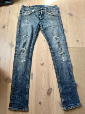  Dondup Jeans - Säljer ett par blå skinny jeans från Dondup med slitna detaljer och snyggt tvättad look. Jeansen har klassisk femficksdesign och dragkedja med knapp. Perfekta för dig som gillar en smal passform och trendiga slitningar. Storlek 31/31