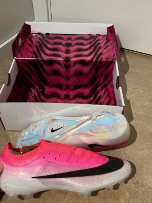 nike mercurial vapor 17 elite fg breakout - rosa/vit/svart - Säljer ett par Nike Mercurial fotbollsskor i en grymt snygg rosa och silverfärgad design med svart swoosh. Skorna har genomskinlig sula och är tillverkade i lätt syntetmaterial med Atomknit-överdel för bästa passform och känsla på planen.