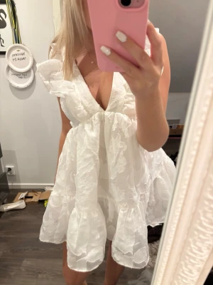 Vit kort klänning med snörning - Söt vit kortklänning med volangdetaljer, djup v-ringning och snörning i ryggen. Klänningen har puffiga korta ärmar. Hade denna på min student 💞💞
