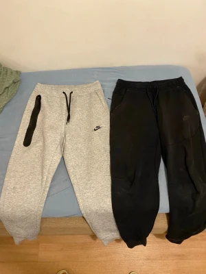 2 par Nike tech svart/ grå  - Svarta mjukisbyxor från Nike med dragsko i midjan och ribbade benslut. Byxorna har sidofickor och en diskret Nike-logga på vänster ben. Perfekta för chill dagar eller träning, tillverkade i mjukt och bekvämt material.