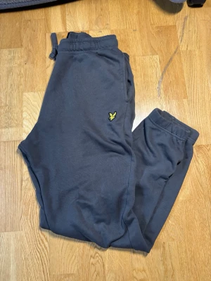 Mörkgrå mjukisbyxor från lyle and scott - Mörkgrå mjukisbyxor från lyle and scott med resår i midjan och benslut, sidofickor och en bakficka. Byxorna har lyle and scott logga på vänster ben och är gjorda i mjukt bomullsmaterial för maximal komfort. Har bara använd ett par gånger, för frågor eller för fler bilder är det bara att skicka ett meddelande!!!!