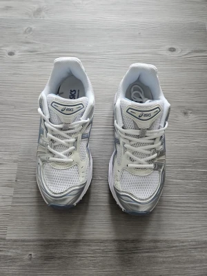 Asics gel kayano 14 - Snygga vita sneakers från Asics med detaljer i silver och ljusblått. Skorna har en sportig design med meshpaneler för bra ventilation och robust sula för skön komfort. Perfekta för dig som gillar en clean och fräsch look till vardags.