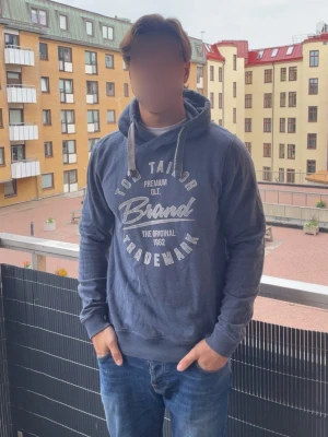 Vintage Tom Tailor hoodie - Mörkblå hoodie från Tom Tailor med tryck på bröstet i vitt och grått. Klassisk modell med huva och dragsnören samt ribbade muddar vid ärmslut och nederkant. Perfekt för en avslappnad och stilren look. Passar M/L, hör gärna av dig vid funderingar och frågor! Modell 190cm