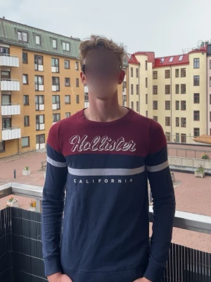 Vintage Hollister tröja - Snygg långärmad tröja från Hollister i marinblått och vinrött med vita detaljer. Tröjan har rund halsringning, tryckt logga och texten 'California' framtill. Perfekt för en avslappnad och trendig vintage stil. Passar XS och S