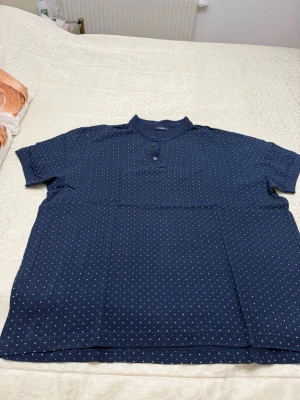 Mörkblå prickig t-shirt LC Waikiki - Snygg mörkblå t-shirt från LC Waikiki i storlek 3XL. T-shirten har korta ärmar, små vita och blå prickar över hela tyget samt en unik krage med knappar framtill. 