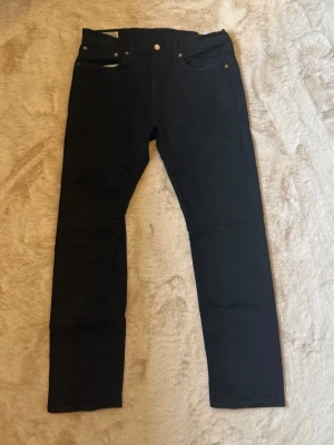 Svarta Levis 502  - Snygga svarta jeans med taperd passform och klassisk femficksdesign. Jeansen har normal midja och är tillverkade i ett stretchigt denimtyg som ger en bekväm känsla. Perfekta för en stilren och enkel look. W34 L32