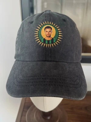 Gustav Lundgren inspirerad GAIS-keps – Vintage Washed | Svart Supporterkeps - Svart vintage washed keps med motiv inspirerat av Gustav Lundgren och GAIS. 🟢⚫️  Avslappnad dad cap-modell med böjd skärm och snyggt urtvättad finish. Motivet framtill gör den till en kul och annorlunda supporteraccessoar för GAISaren.  🟢 Gustav Lundgren-inspirerat motiv ⚫️ Svart vintage washed finish 🧢 Klassisk dad cap-passform 📏 Justerbar baktill 👤 Unisex Nyskick 