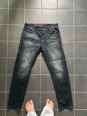 Mörkblå raka jeans med slitningar - Snygga mörkblå jeans med raka ben och diskreta slitningar på framsidan. Klassisk femficksmodell med knappgylf och kontrastsömmar. Jeansen har en tvättad look som ger en avslappnad vibe och passar perfekt till vardagsstilen.