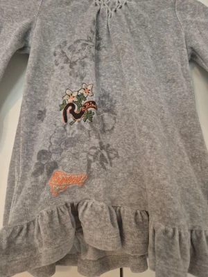 Grå hoodieklänning med volang - Supersöt grå hoodieklänning från Replay med volangkant nedtill och broderade detaljer framtill. Långärmad modell med huva och mjukt material som känns skönt mot huden. Perfekt för en chill och trendig look. storlek 24 månader (motsvarar cirka storlek 86/92)