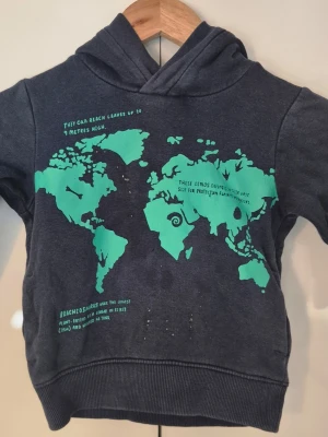 Mörkblå hoodie med världskarta - Cool mörkblå hoodie med huva och tryck av en grön världskarta och dinosauriefakta på framsidan. Hoodien har långa ärmar och ribbade muddar vid ärmslut och nederkant. Perfekt för dig som gillar unika prints och bekväma plagg. i storlek 92