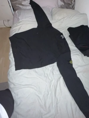 Svart hoodie från Stone Island - Säljer en svart hoodie från Stone Island med den klassiska loggan på vänster ärm. Hoodien har en avslappnad passform och är tillverkad i mjukt bomullsmaterial. Perfekt för dig som gillar streetwear och vill ha en stilren look.