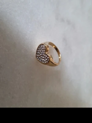 Pilgrim emmett ring med hjärta och stenar - Snygg guldpläterad ring från pilgrim med ett hjärtformat motiv täckt av glittrande precisa kristaller. Ringen är justerpar och passar alla. Superfin!! Men kommer inte till användning🥺💗
