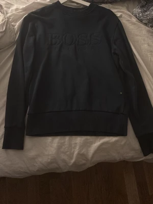 Mörkblå  sweatshirt från BOSS - Stilren mörkblå sweatshirt från BOSS med diskret broderad logga framtill. Tröjan har rund halsringning, långa ärmar och breda muddar vid ärmslut och nederkant. Perfekt för en clean och avslappnad look.