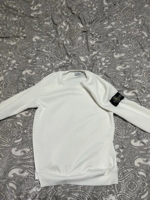 Vit hoodie från Stone Island - Säljer en clean vit hoodie från Stone Island med den klassiska svarta patchen med gul logga på vänster ärm. Hoodien har rund hals, ribbade muddar och är gjord i mjukt material som känns riktigt skönt mot huden. Perfekt för dig som gillar streetwear och vill ha något stilrent. Passar som xs