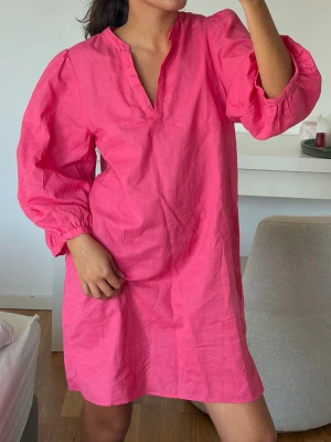 Rosa klänning  - En enkel och snygg kort klänning i stark rosa färg. Klänningen har v-ringad hals, ballongärmar med resår vid ärmslut och en loose passform. 