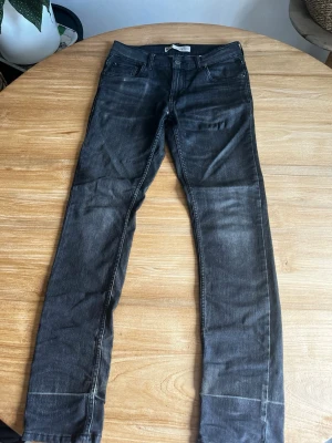 Svarta slim fit jeans - Snygga svarta slim fit jeans med klassisk femficksdesign och dragkedjegylf. Jeansen har en tvättad look med lätt slitna detaljer och raka ben. Perfekta till en avslappnad streetstyle eller vardagsoutfit.
