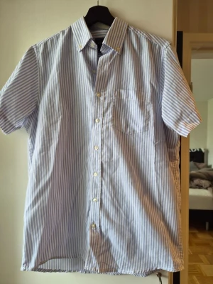 Blårandig kortärmad skjorta Signal - Kortärmad skjorta från Signal i ljusblått och vitt med klassiska vertikala ränder. Skjortan har knappar framtill, bröstficka och button down-krage. Perfekt för en avslappnad och stilren look.