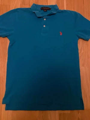 Blå pikétröja från u.s. Polo Assn. - Snygg blå pikétröja från u.s. Polo Assn. med klassisk krage, två knappar och den ikoniska röda loggan broderad på bröstet. Tillverkad i bomull som känns skön mot huden. Perfekt till jeans eller shorts för en clean look.
