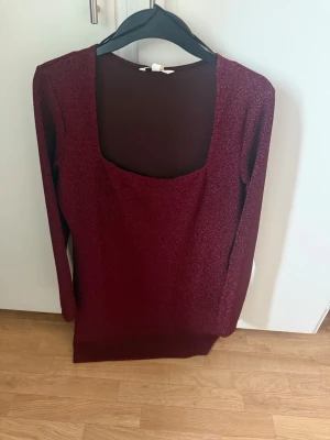 Ny Vinröd glittrig långärmad klänning strl L - Vinröd kortklänning med glittrigt tyg och lång ärm. Klänningen har en djup, fyrkantig urringning och är figurnära i modellen. Perfekt för dig som vill sticka ut med en elegant och trendig look.